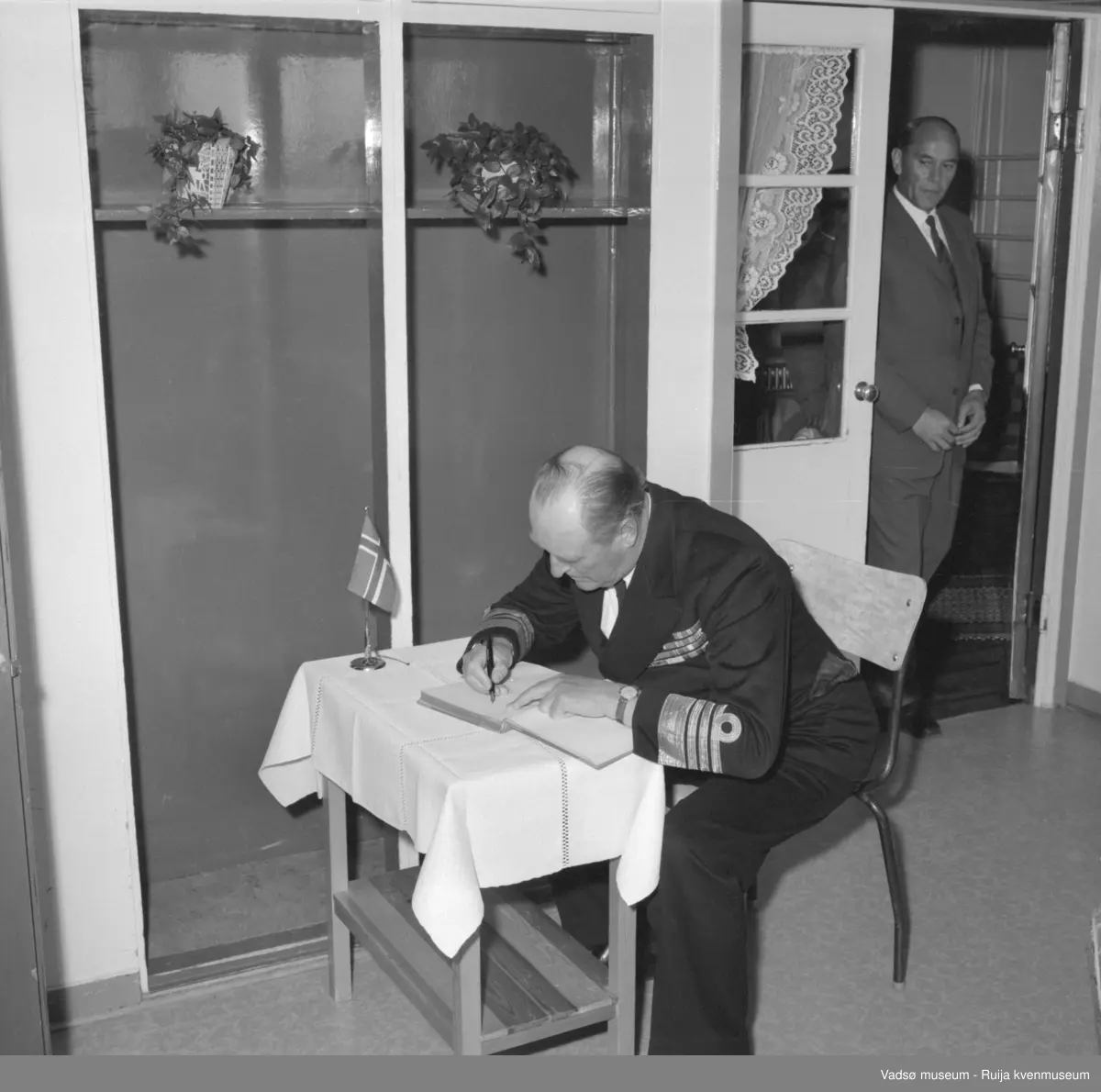 Vestre Jakobselv juli 1959. Kongebesøk på barnehjemmet Vårsol. Kong Olav signerer besøksprotokoll. I døråpningen ordfører Henry Karlsen.