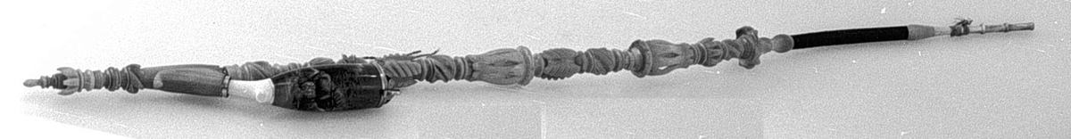 Langpipe i tre deler: Piperør, pipehode og munnstykke. Pipehodet av porselen  er påmalt et skogmotiv med en elg, og harr lokk av sølv. Piperøret og munnstykket er av utskåret alabast. Det midtertste partiet på munnstykket er bøyelig.