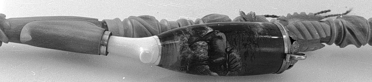 Langpipe i tre deler: Piperør, pipehode og munnstykke. Pipehodet av porselen  er påmalt et skogmotiv med en elg, og harr lokk av sølv. Piperøret og munnstykket er av utskåret alabast. Det midtertste partiet på munnstykket er bøyelig.