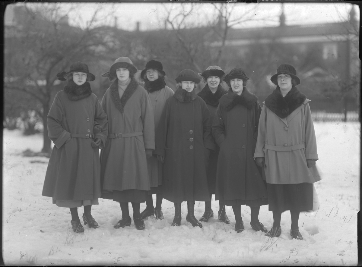 Gruppbild med sju kvinnor klädda i vinterkappor och hattar fotograferade ute i snön. Längst till vänster står Lilly Johansson och kvinnan tredje från höger heter Lisa (efternamn okänt).