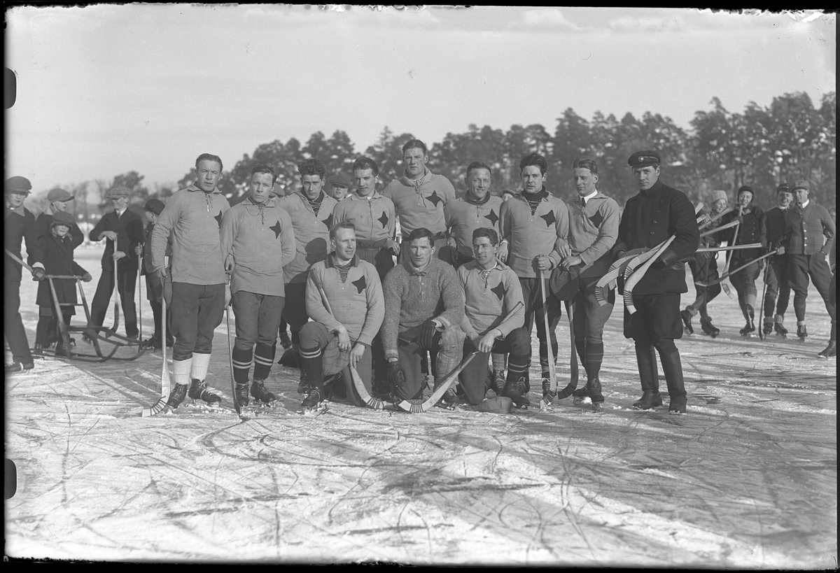 Gruppbild på Vänersborgs bandylag uppställda på isen. I bakgrunden står barn med bandyklubbor.