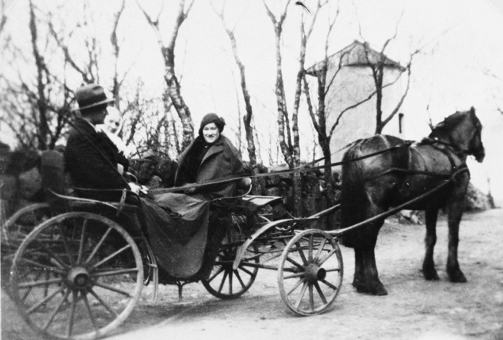 Bolette Henrikke Hognestad f. Seland, sonen Steinar Hognestad og Tone Hognestad i trilla på veg til kyrkje. I bakgrunnen eple(potet)rev siloen.