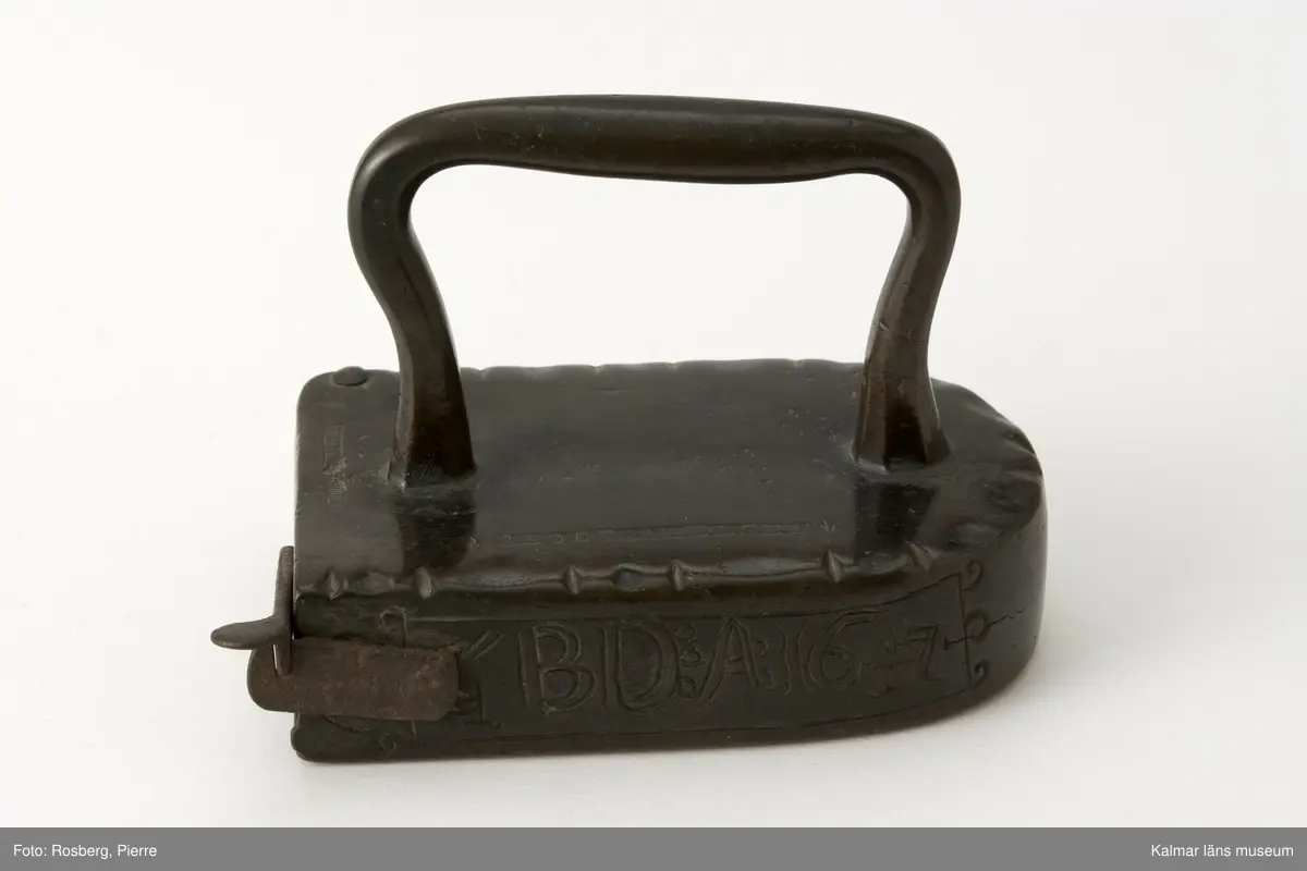KLM 5926. Stykjärn. Av malm. Avsett för lod. Lucka baktill. Framtill rundat. Handtaget av malm. Text på smalsidan inom en ram: G.B.D.A:1647, på uppsidan inpunsat: PEDER NIELSEN. Luckan ornerad med halvmånformiga ornament,