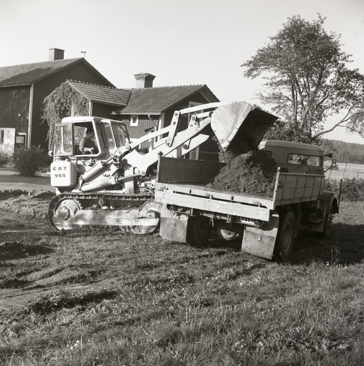 En man lastar jord på ett lastbilsflak med en grävmaksin vid gården Sunnanåker, 1967.