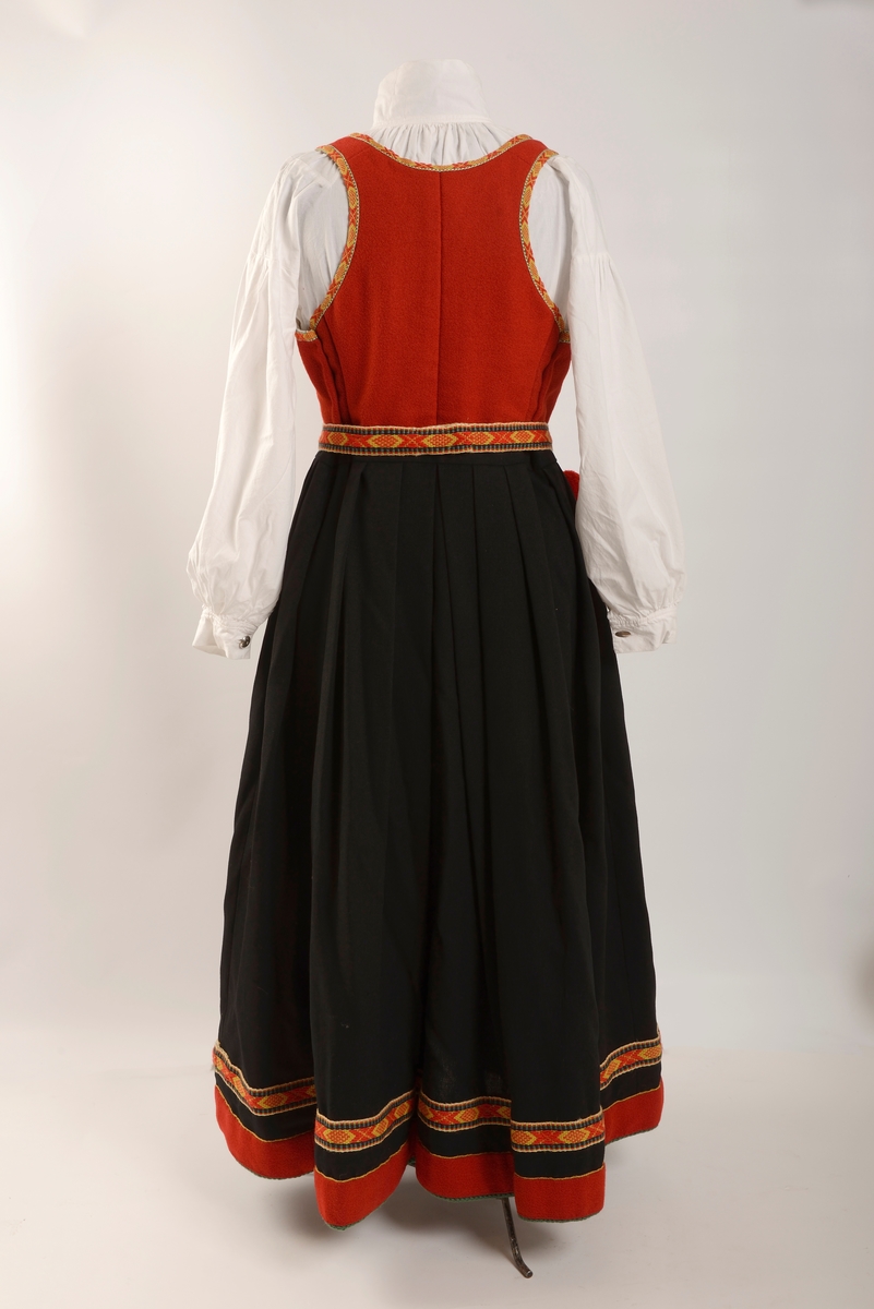 Kvinnebunad fra Vestfold, 1956 - modell.

Giver og tidligere eier, Wenche Blomberg, har fortalt dette om bunaden: 
"Vestfoldbunaden omtales i Norsk bunadleksikon b. 2, min er 1956-modellen avbildet på s.99.Jeg kjøpte den brukt på 1970-tallet en gang. Selgeren hadde sydd den selv og initialene hennes står på et lite metallmerke som er festet på innsida av capen. Husker ikke navnet. Hun bodde på Nøtterøy-sida av Kanalbrua i Tønsberg. Den passet akkurat, så jeg slapp å bruke penger på tilpassing. Jeg bare sydde på et par ekstra smålommer på den grønne understakken etter en tid. Bortsett fra snøringslenka som fulgte med, kjøpte jeg det øvrige sølvet sjøl. Lue og sko likeså. Etter noen år med heftig dansing der lua hele tida føyk av fordi jeg ikke likte å bruke hakeknyting, sydde jeg på en borrelås-strimmel inni, og da satt den bedre fast i håret. Ekstra bomullsskjorte kjøpte jeg seinere på Husfliden i Tønsberg.
 
Brukte den lite de første åra, men da jeg kom tilbake til Oslo i 1985 etter fem år i Nord-Gudbrandsdalen og etterhvert ble leikarring-aktiv, økte bruken betraktelig. I skjørtet er det ei lita rift som jeg rev opp da jeg klatra over et nettinggjerde i hagen utafor bygningen som tidligere huset Norges geografiske oppmåling, seinere Kunstakademiet, der det ofte var forskjellige festlige arrangementer. Jeg husker ikke anledningen og hvorfor jeg ble hengende fast i det gjerdet, men skaden var ikke større enn at jeg reparerte den sjøl. Pompongene på forklesnora var ellers et sårt punkt, måtte få noen til å lage nye for meg en gang, men jeg husker ikke hvem som gjorde det - kanskje Husfliden ett eller annet sted. Låsen på lauslomma var også til stadig irritasjon fordi den sprang opp hele tida så tobakken min datt ut.

Når man er folkedanser er skoa nærmest hjertet! Disse skoa var til slutt så godt inntrødde at jeg kvidde meg for å bruke et par nye jeg kjøpte via BUL. (Forresten: Hvilket par fikk dere? De gamle slitte, eller de nye? Begge?) [Opplysning fra Kvinnemuseet: Bare de nye skoene er del av gaven]

Seinere på 80-90-tallet en gang fikk jeg lagt stakken ut i livet av systova på Heimen. De bildene jeg har funnet er fra tida i Leikarringen i BUL. Det er forresten ikke lett å ri med bunadsstakk, kan jeg meddele. Hvor skal man gjøre av alt stakkestoffet der man sitter overskrevs? 

Jeg brukte bunaden siste gang 17. mai 2017 i Svullrya. Da hadde den krympa så mye at jeg knapt fikk den på meg, og nå så jeg ingen grunn til å bruke mer penger på utvidelser."

Til bunaden hører også to jakkemerker, ett fra Noregs ungdomslag, NU, og ett med symbol av en drage, som er merket for mikrostaten Ladonia, der Wenche Blomberg er Minister of Madness og Enkegrevinne Wenche von Blomberg und Grünerløkka. 

Om det siste merket forteller Wenche Blomberg: 
"Ladonia: Virtuell ministat opprettet av kunstneren Lars Vilks. Det finnes en god del slike på nettet, men Ladonia er i tillegg knyttet til et konkret geografisk område ved Kullen i Skåne: ei nesten utilgjengelig strandstripe av kjemperullestein der Vilks har bygd opp en rekke monumentale skulpturer av rekved. Historie, bilder etc på www.ladonia.org. Det har forekommet åratals med fornøyelige tvister med grunneiere og staten Sverige. Alle kan bli borgere av Ladonia, noe som fra tid til annen har ført til massehenvendelser fra en del land i Asia fra folk som vil emigrere og søker visum. Statsbudsjettets inntektsside stammer i stor grad fra salg av titler. Det var sånn jeg ble enkegrevinne og står i adelskalenderen. Man kan foreslå seg selv til minister for et hvilket som helst fantasirikt fagområde, men dette må godkjennes av regjeringen. Det var ingen innvendinger mot min søknad om å bli «minister of madnesss", man fant at den passet utmerket inn."