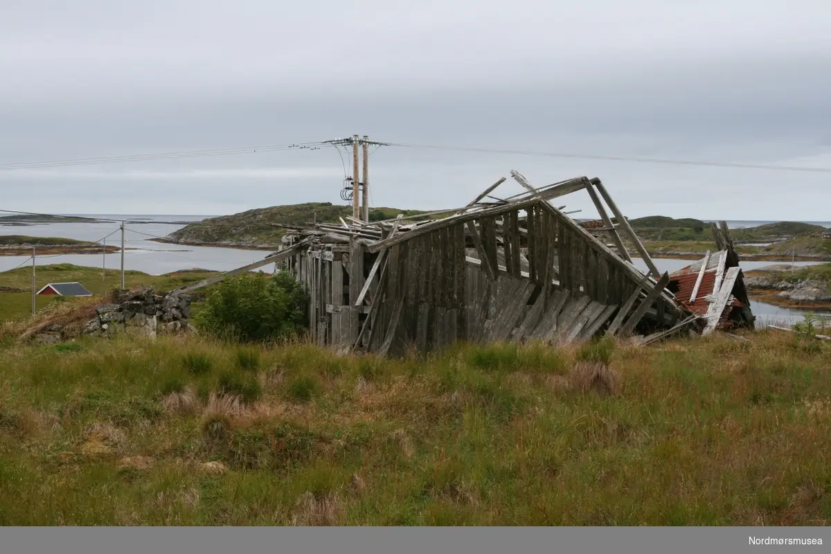 Serie Kmb-2018-010.0001-0092: "Arresten på Tingvoll som ble losjihus og seinere fjøs på Veiholmen."

Serie fotos som viser hovedsaklig ruinene av det gamle "Nordmøre Arresthus". Lokalisert på et gårdsbruk på Nordre Skomsøy i Smøla kommune - nærmere bestemt på Gnr. 41 Bnr. 5. Dette bruket ble skilt ut fra Bnr. 1 i 1916, men skjøtet ble ikke tinglyst før 22. september 1924. Det var Andreas Olsen Skomsøy som fikk skjøte fra sin far, Ole Bersvendsen Skomsøy. I 1926 bygde Andreas hus på Bnr. 5, og det fikk også navnet "Nordre Skomsøy". 

Andreas Olsen Skomsøy kjøpte losjihuset "Arresten" på Innerklakken på Veiholmen og flyttet dette til Nordre Skomsøy. "Arresten" bestod delvis av tømmerkroppen av det tidligere arresthuset for Nordmøre Fogderi på Tingvoll, som ble lagt ned og solgt på auksjon etter at det nye distriktsfengselet i Kristiansund ble tatt i bruk 1. april 1865. Det gamle arresthuset i tømmer ble revet og flyttet til Veiholmen. Væreier Ole Daniel Rognskog bygde i 1870-årene fem store og ett mindre losjihus på Veiholmen for tilreisende fiskere under skreifisket. "Arresten" var ett av disse.

Det tidligere losjihuset ble satt opp som fjøs på Nordre Skomsøy i 1925-27. Tømmerkroppen av det gamle arresthuset utgjorde en del av fjøset, og ble forlenget med et tilbygg i reisverk på 5,3 m lengde. I 1927-35 ble fjøset panelt utvendig og påbygd en toppetasje som låve. 

Bygninga står nå (2018) til nedfalls. Tømmerkroppen av det gamle arresthuset er likevel godt synlig. Det ser ut til å ha vært en solid bygning – vi kan tydelig se at tømmerstokkene har vært låst sammen på en spesiell måte. Vinduene til arrestrommene var nok i sin tid helt annerledes enn de vindusåpningene vi ser i dag – sannsynligvis glugger/lysåpninger høyt på veggen med noen ti-talls cm høyde og bredde. Endeveggen vi ser på bildene vendte mest sannsynlig sydover mot Tingvollvågen da arresthuset lå på Bekken. Motsatt endevegg med inngangen til arresthuset vendte mest sannsynlig mot nord.

Andre bygninger vi ser i denne serien (KMb-2018-010.0001-0092) er det røde våningshuset på gårdsbruket, samt det grå sjøhuset. Det hvite huset vi ser på noen av bildene i serien, er huset som ble satt opp på tomta hvor "Arresten" tidligere hadde stått på Innerklakken på Veiholmen. Statens havnevesen satte i midten av 1930-årene opp et forlegnings- og messehus for arbeidere under havnearbeidene som ikke var fra Veiholmen. I 1938 ble denne eiendommen skjøtet over fra Hopen kommune til Veiholmen Sanitetsforening – det kalles "Sanitetsheimen" – og står der den dag i dag.

Andreas Olsen Skomsøy døde i 1968. Kona hans, Augusta Kristine Olsdotter Ersnes, døde i 1973. Deres sønn Oddmund Osvald Skomsøy fikk skjøte på Nordre Skomsøy i 1974. Hans sønn Odd Gunnar Skomsøy fikk skjøte på Nordre Skomsøy i 1988, mot bruk og disposisjonsrett til foreldrene. 

Fotograf og informasjon: Knut Even Isaksen. Kjentmann under besøket var Bjørn Ivar Hannasvik. Eier av de originalmaterialet er Knut Even Isaksen. Bildene er gitt i digital gave til Nordmøre museum. Fra Nordmøre museums fotosamlinger.