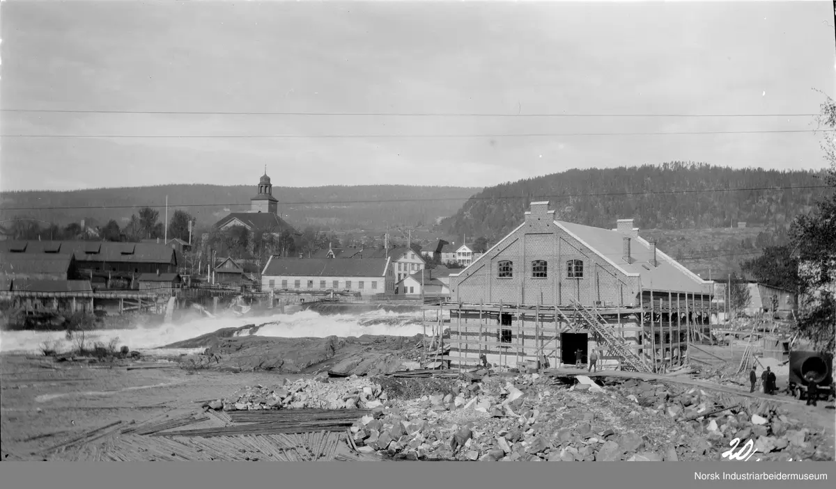 Tømmer i vannet ved Nybrufossen i Kongsberg. Smeltehytta, Kongsberg kirke, den kongelige mynt og kraftverket i Nybrufossen sees.