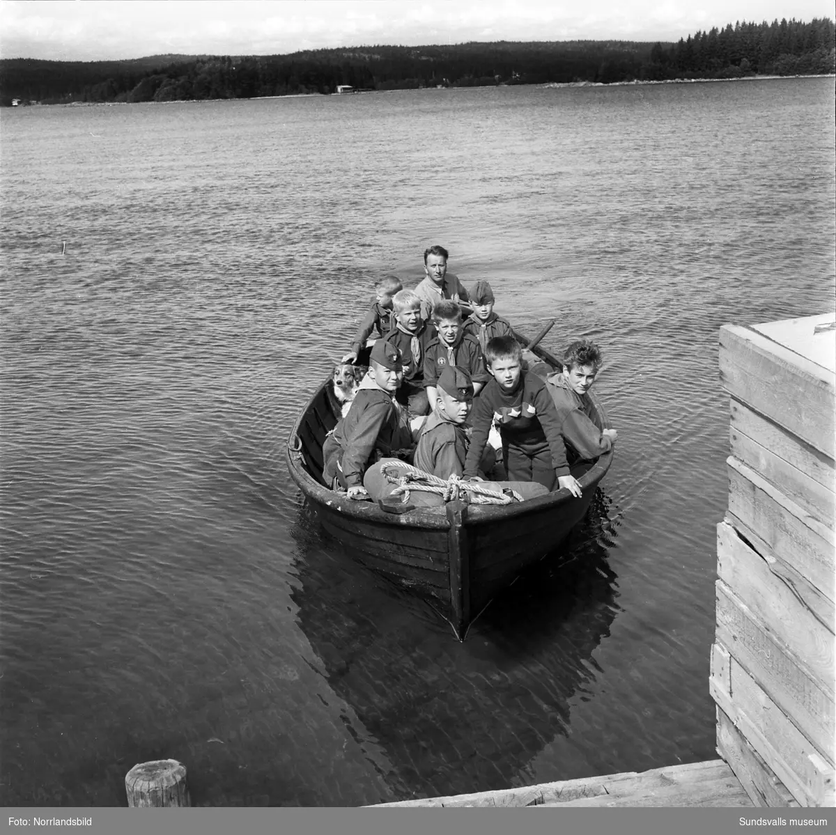 I juli 1959 anordnade Svenska Scoutförbundet sitt stora internationella läger på Rödön utanför Alnö. På första bilden ses lägerledaren Tage Allegård anlända med en grupp pojkscouter för några intensiva veckor på ön. Lägret hade förberetts under ett helt år och dagarna innan hade 70 pojkscouter och ledare hjälpts åt att bygga upp de olika lägerbyarna, som fick namn efter olika fyrar.  SCA hade upplåtit en pråm som låg för ankar i hamnen fylld med de matvaror som krävdes för att mätta de cirka 800 deltagarna.