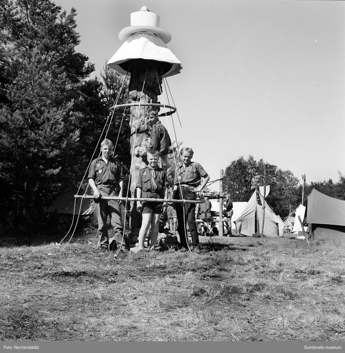 I juli 1959 anordnade Svenska Scoutförbundet sitt stora internationella läger på Rödön utanför Alnö. På första bilden ses lägerledaren Tage Allegård anlända med en grupp pojkscouter för några intensiva veckor på ön. Lägret hade förberetts under ett helt år och dagarna innan hade 70 pojkscouter och ledare hjälpts åt att bygga upp de olika lägerbyarna, som fick namn efter olika fyrar.  SCA hade upplåtit en pråm som låg för ankar i hamnen fylld med de matvaror som krävdes för att mätta de cirka 800 deltagarna.