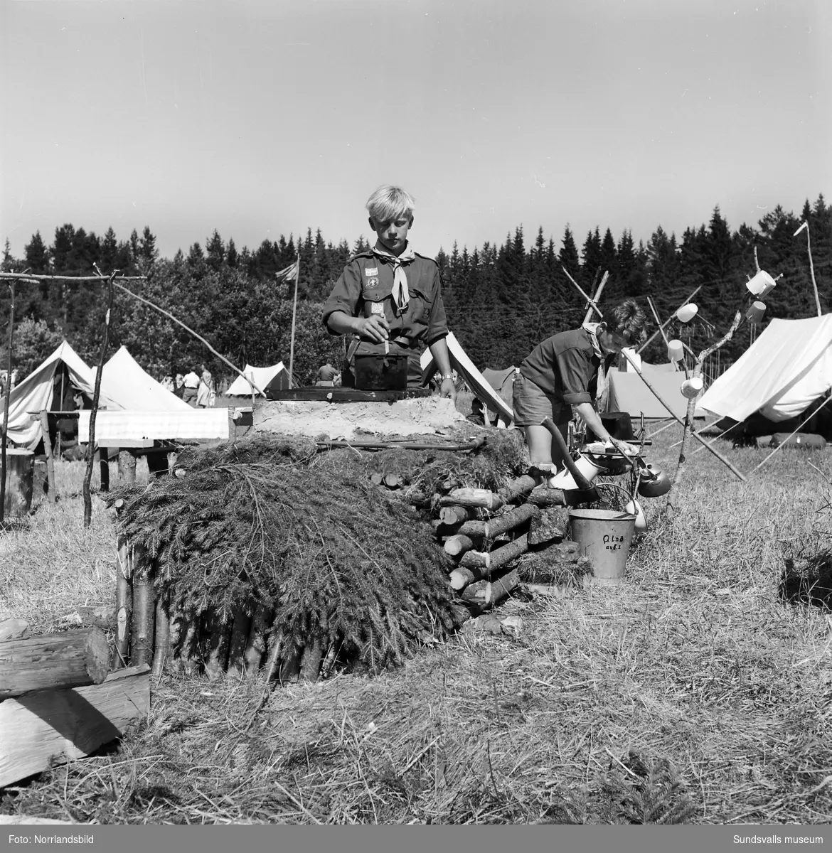 I juli 1959 anordnade Svenska Scoutförbundet sitt stora internationella läger på Rödön utanför Alnö. På första bilden ses lägerledaren Tage Allegård anlända med en grupp pojkscouter för några intensiva veckor på ön. Lägret hade förberetts under ett helt år och dagarna innan hade 70 pojkscouter och ledare hjälpts åt att bygga upp de olika lägerbyarna, som fick namn efter olika fyrar.  SCA hade upplåtit en pråm som låg för ankar i hamnen fylld med de matvaror som krävdes för att mätta de cirka 800 deltagarna.