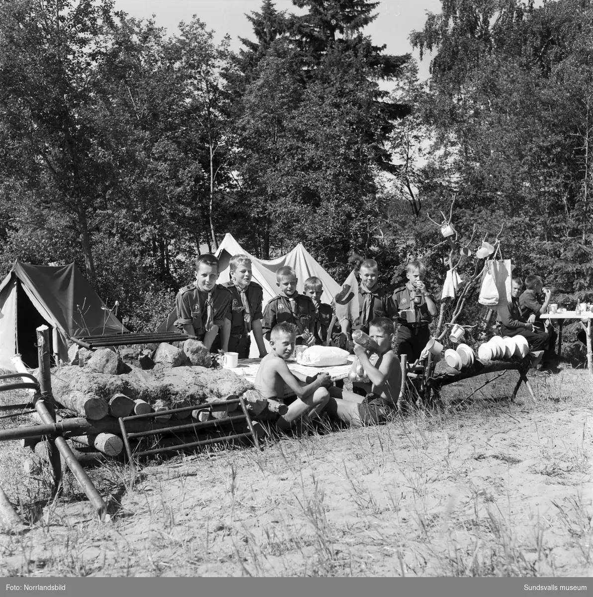 I juli 1959 anordnade Svenska Scoutförbundet sitt stora internationella läger på Rödön utanför Alnö. På första bilden ses lägerledaren Tage Allegård anlända med en grupp pojkscouter för några intensiva veckor på ön. Lägret hade förberetts under ett helt år och dagarna innan hade 70 pojkscouter och ledare hjälpts åt att bygga upp de olika lägerbyarna, som fick namn efter olika fyrar.  SCA hade upplåtit en pråm som låg för ankar i hamnen fylld med de matvaror som krävdes för att mätta de cirka 800 deltagarna.