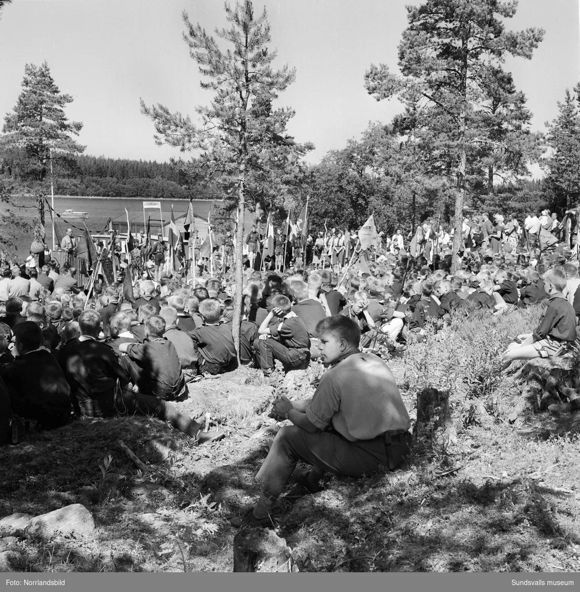 I juli 1959 anordnade Svenska Scoutförbundet sitt stora internationella läger på Rödön utanför Alnö. På första bilden ses lägerledaren Tage Allegård anlända med en grupp pojkscouter för några intensiva veckor på ön. Lägret hade förberetts under ett helt år och dagarna innan hade 70 pojkscouter och ledare hjälpts åt att bygga upp de olika lägerbyarna, som fick namn efter olika fyrar.  SCA hade upplåtit en pråm som låg för ankar i hamnen fylld med de matvaror som krävdes för att mätta de cirka 800 deltagarna.