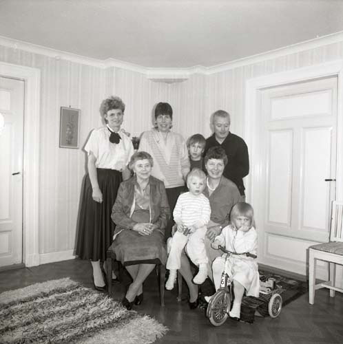 En grupp med både barn och vuxna poserar för ett fotografi. En flicka sitter på en trehjuling och lutar sin haka i ena handen, 1985.