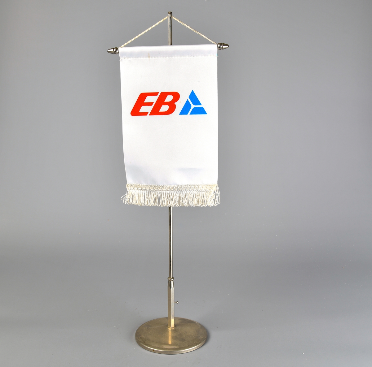 Bordvimpelen er rektangulær. Overkanten er omsydd, og en metalltang med kjegleformede avslutninger er stukket gjennom. EVed vimpelens underkant er det påsydd et hvit frynsebånd. Det er kun en side av vimpelen som har logo påtrykket.

Den hvite tråden øverts på vimpelen brukes til å henge den i et bordstand bestående av et sølvfarget metallstang som er skrudd fast i en rund fot. Grønn filt limt på undersiden. Mulgens en toppdel som holder tråden på plass som er forsvunnet.