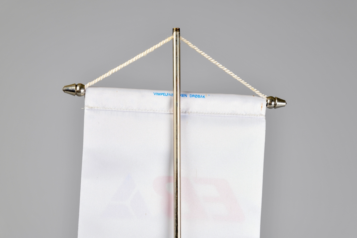 Bordvimpelen er rektangulær. Overkanten er omsydd, og en metalltang med kjegleformede avslutninger er stukket gjennom. EVed vimpelens underkant er det påsydd et hvit frynsebånd. Det er kun en side av vimpelen som har logo påtrykket.

Den hvite tråden øverts på vimpelen brukes til å henge den i et bordstand bestående av et sølvfarget metallstang som er skrudd fast i en rund fot. Grønn filt limt på undersiden. Mulgens en toppdel som holder tråden på plass som er forsvunnet.