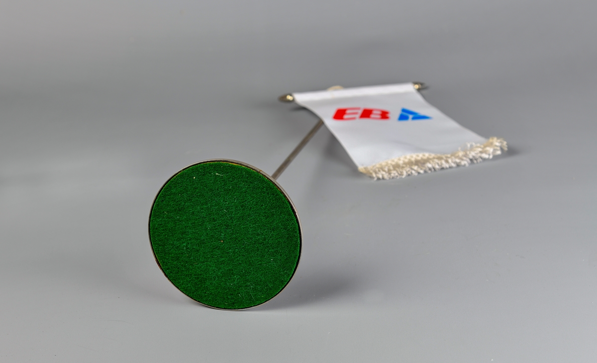 Bordvimpelen er rektangulær. Overkanten er omsydd, og en metalltang med kjegleformede avslutninger er stukket gjennom. EVed vimpelens underkant er det påsydd et hvit frynsebånd. Det er kun en side av vimpelen som har logo påtrykket.

Den hvite tråden øverts på vimpelen brukes til å henge den i et bordstand bestående av et sølvfarget metallstang som er skrudd fast i en rund fot. Grønn filt limt på undersiden. Mulgens en toppdel som holder tråden på plass som er forsvunnet.