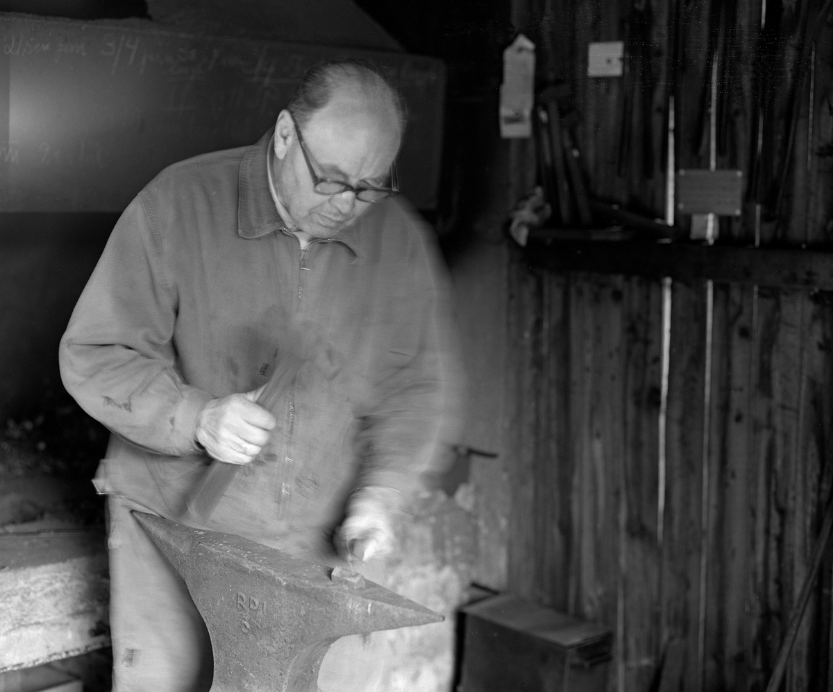 Knivmakeren Even Johannes Blindingsvolden (1908-1985) fra Ringsaker, fotografert ved ambolten i smia, der han bearbeidet varmt knivblademne med en hammer mens han holdt det med ei tang.  Den på dette tidspunktet 65 år gamle håndverkeren var kledd i dongeriklær mens han arbeidet.  Blindingsvolden eide og bodde på småbruket Rudsland på Rudshøgda.  Her hadde han et et 43 kvadratmeter stort hus ved Prestvegen som inneholdt smie- og verkstedrom.

Mer informasjon om knivsmeden Even Blindingsvolden finnes under fanene «Bildehistorikk» og «Opplysninger».