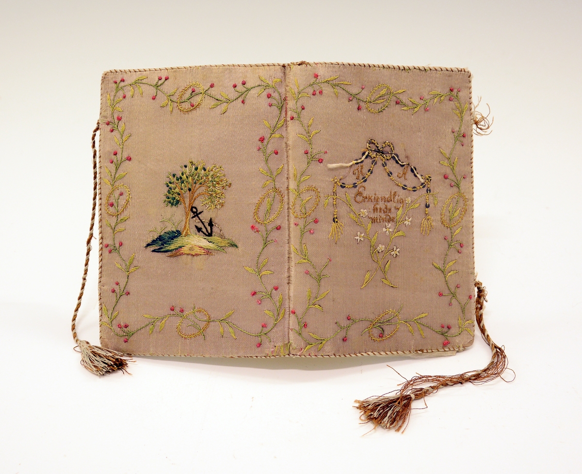 Lommebok i silke med brodert motiv og tekst. Innvendig med tre rom. Permane paaføra med gult og violet silkety med blomebrodering  paa utsidane. Paa framsida stend sauma: H.A. - Erkjendlighedsminde. Paa baksida eit tre, innaat dette eit ankar. Tvunnet silkeband.
