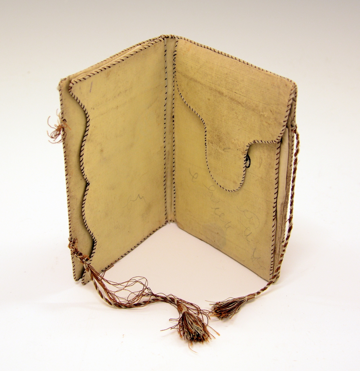 Lommebok i silke med brodert motiv og tekst. Innvendig med tre rom. Permane paaføra med gult og violet silkety med blomebrodering  paa utsidane. Paa framsida stend sauma: H.A. - Erkjendlighedsminde. Paa baksida eit tre, innaat dette eit ankar. Tvunnet silkeband.