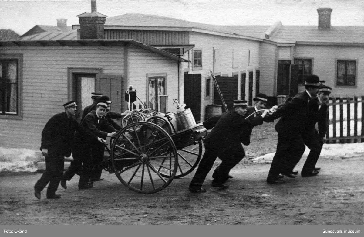 Brandmän som drar en brandvagn upp för en brant backe, troligen Södermalm. Ur album från brandchefen för Sundsvalls brandkår Gustaf Hellgren och hans familj.