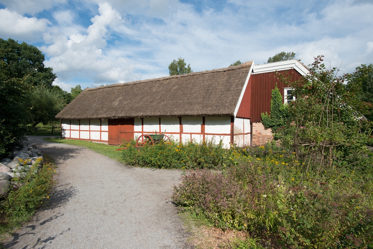 Den västra loglängan på Skånegården är uppförd i en våning i korsvirkesteknik, där facken är fyllda med lerklining på stakar och flätverk. Virket är struket med röd slamfärg och fyllningarna är kalkade på fasadytorna. Den äldre grunden av natursten byttes 1925 mot en betongsockel, denna återskapades vid flytten till Skansen. Byggnaden har ett sadeltak klätt med halm.

 Västra loglängan flyttades till Skansen 1974 från gården Hög 18:1, Högs socken i Skåne.