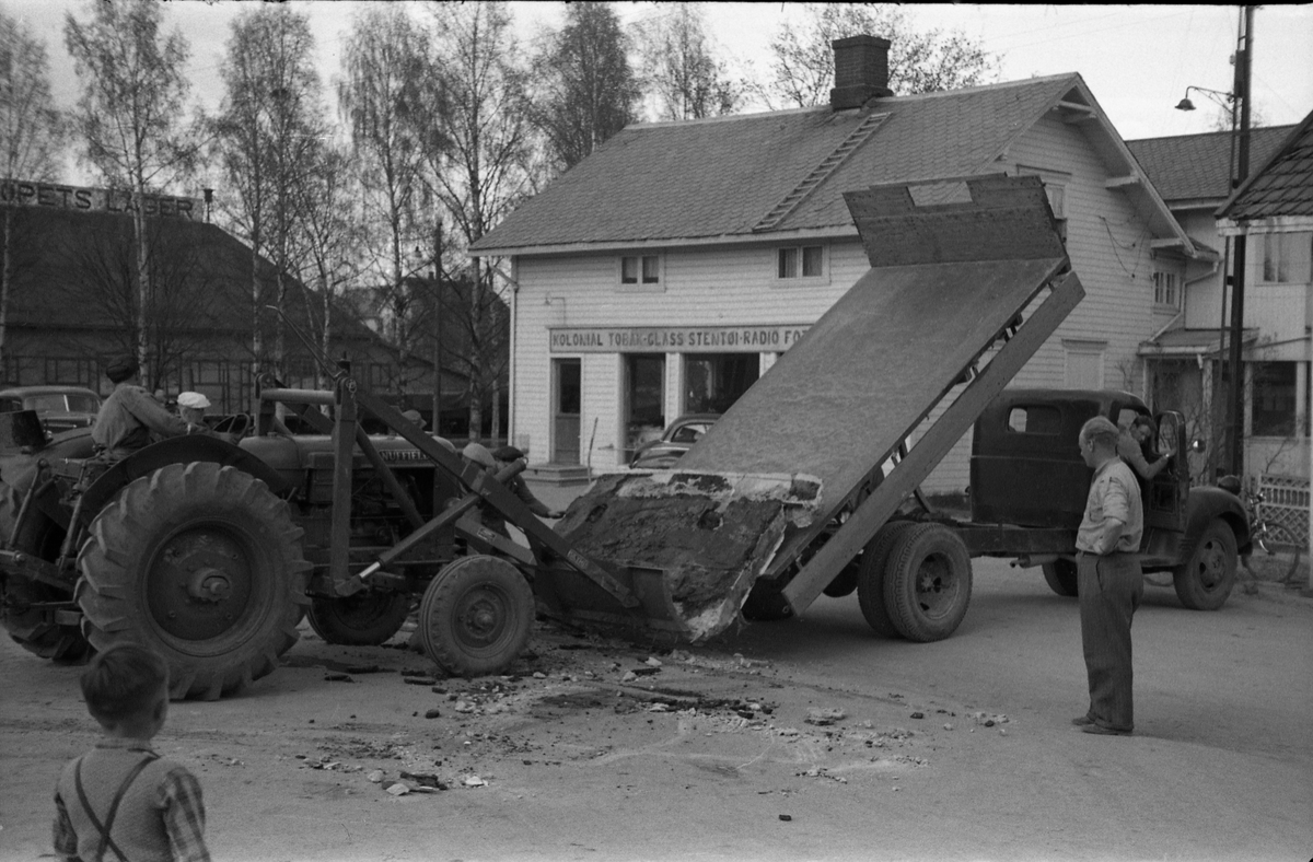 En lasteoperasjon i Lena sentrum april/mai 1954. Har trolig sammenheng med ombygging av Esso bensinstasjon, og det som man strever med å få opp på lastebilen er trolig noe fra rivingen. På bilde nr. fire kan en tydelig kjenne Paul Grindvoll med skyggelue, ellers er ingen av personene identifisert.
