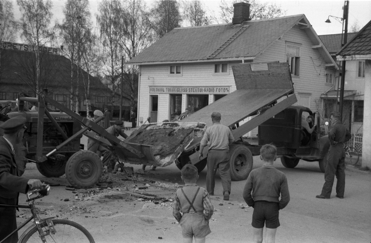 En lasteoperasjon i Lena sentrum april/mai 1954. Har trolig sammenheng med ombygging av Esso bensinstasjon, og det som man strever med å få opp på lastebilen er trolig noe fra rivingen. På bilde nr. fire kan en tydelig kjenne Paul Grindvoll med skyggelue, ellers er ingen av personene identifisert.
