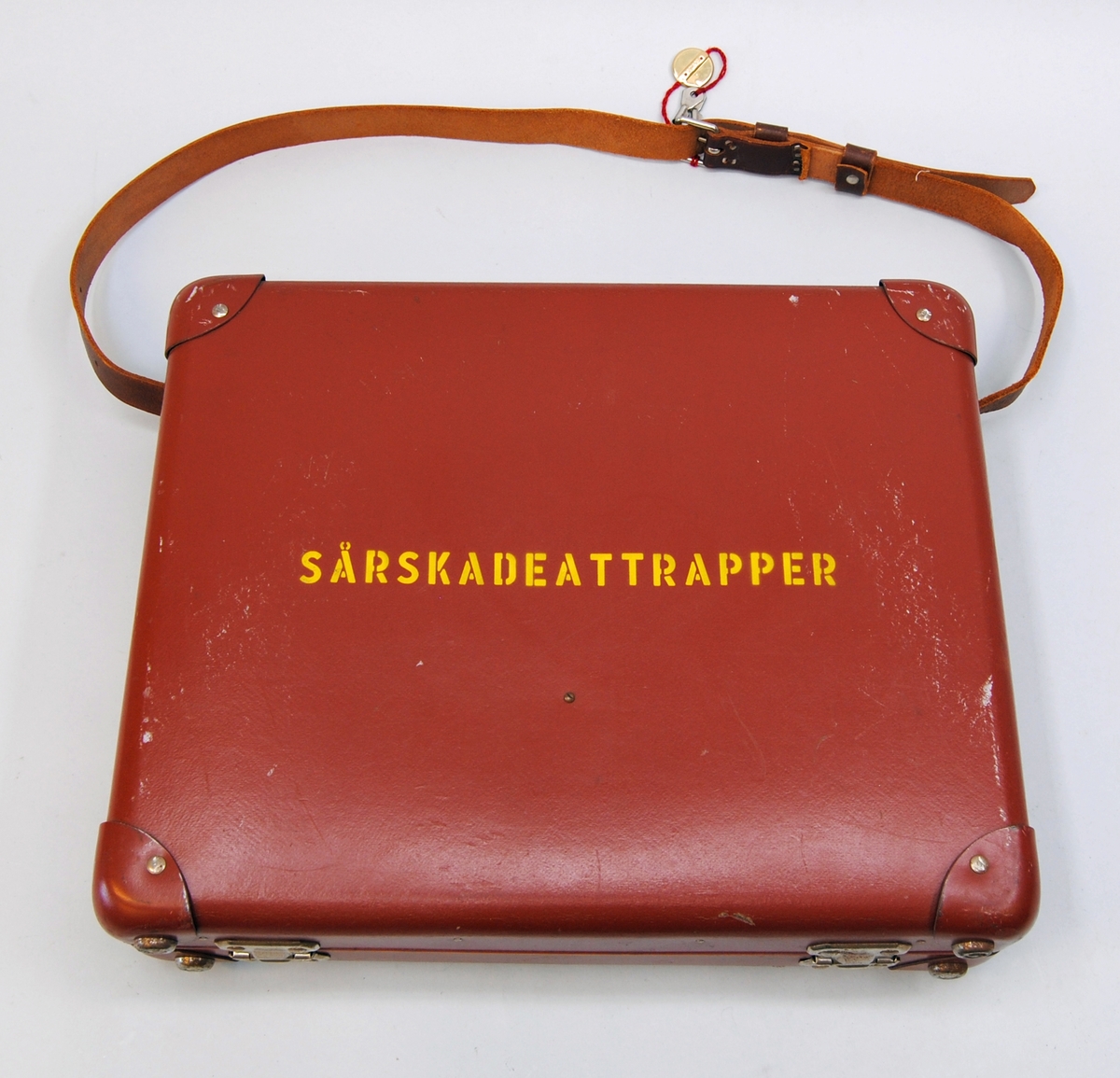 En utbildningsväska av handkofferttyp, gjord av hårdpapp och lackad i roströd färg. På väskans sidor sitter läderförstärkningar i form av infärgat läder fastsatta med metallnitar. Väskan har axelband av brunt läder samt två låsbara lås av metall. Två nycklar i rött band hänger på axelbandet, på bandet återfinns en "metallsigill" med märkningen "Aktiebolaget Tidan Unica Mariestad".
Väskan är inredd med en träram klädd i rutigt papper. Den övre inredningen består av två fackdelar av trä, även det i roströd färg. De övre facken består av sex olika fack, den nedre av två större. Facken är märkta med siffror i gult tryck.
Väskan har även två spännband för att innehållet ska hållas på plats.

Väskan innehåller 25 stycken sårattrapper av gummi som imiterar diverse skador. 
1 för ansikte (:1)
1 för öra (:2)
1 för hand (:3)
2 för fot (:4-5)
20 stycken för oidentifierbara delar av kroppen. (:6-25)
1 kuvert med innehåll (:26)
1 väska (:27) 
6 lappar med beskrivning av de olika skadorna finns för att fästa på attrapperna. Varje attrapp har en märkning i form av nummer som sätts ihop med lapparna. En av attrapperna har tillverkarnamn tryckt på baksidan. Det finns också gummiband, resårband och metallhyskor för fästning av attrapperna i lådan, liggandes i ett kuvert märkt med tillverkarnamn. Handledningsmanual från Röda Korset återfinns det med.