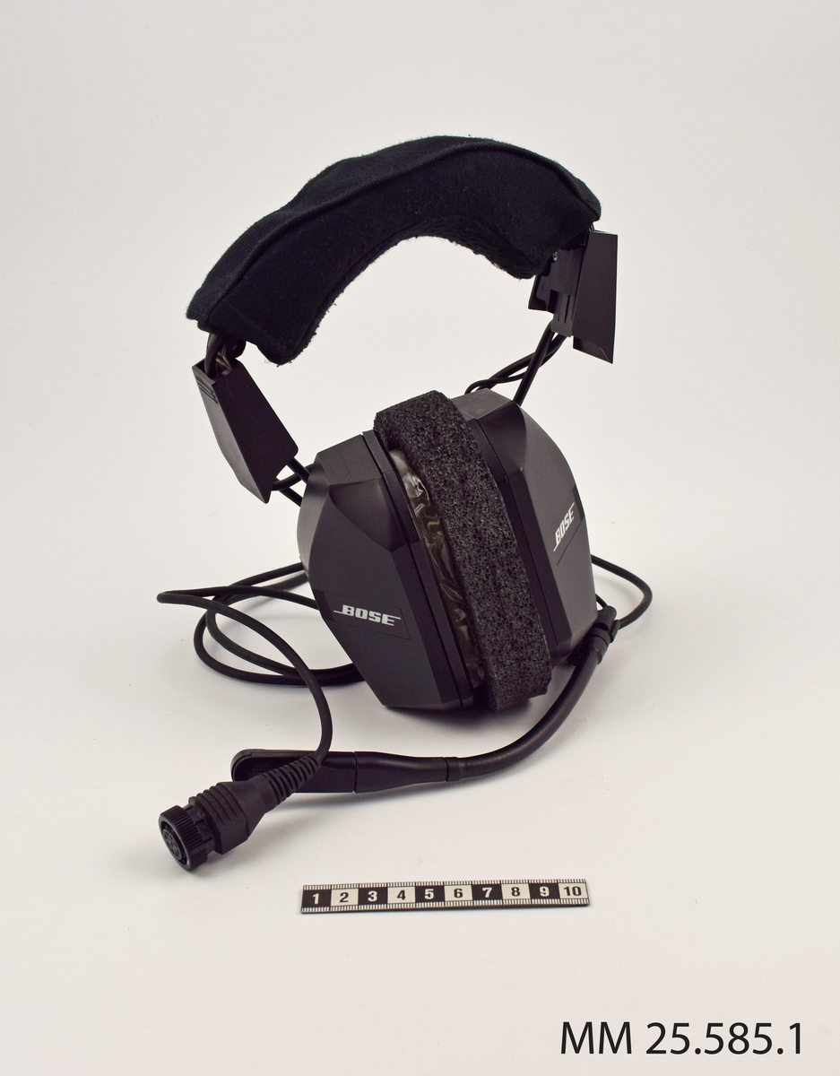 Headset till ubåtsjaktflygplan. Svarta, huvudsakligen tillverkade i plast. Lurarna är försedda med logotyp "BOSE". Från vänster hörlur sitter en mikrofon på en justerbar pinne. En svart sladd kontakt löper från höger hörlur. På baksidan är hörlurarna försedda med genomskinlig plast vilket gör att innanmätet syns.