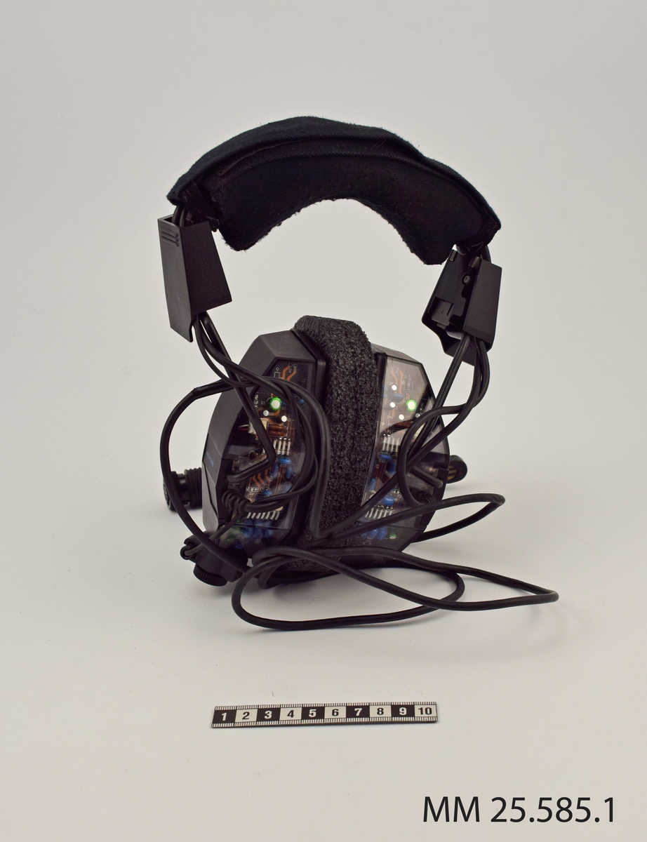 Headset till ubåtsjaktflygplan. Svarta, huvudsakligen tillverkade i plast. Lurarna är försedda med logotyp "BOSE". Från vänster hörlur sitter en mikrofon på en justerbar pinne. En svart sladd kontakt löper från höger hörlur. På baksidan är hörlurarna försedda med genomskinlig plast vilket gör att innanmätet syns.