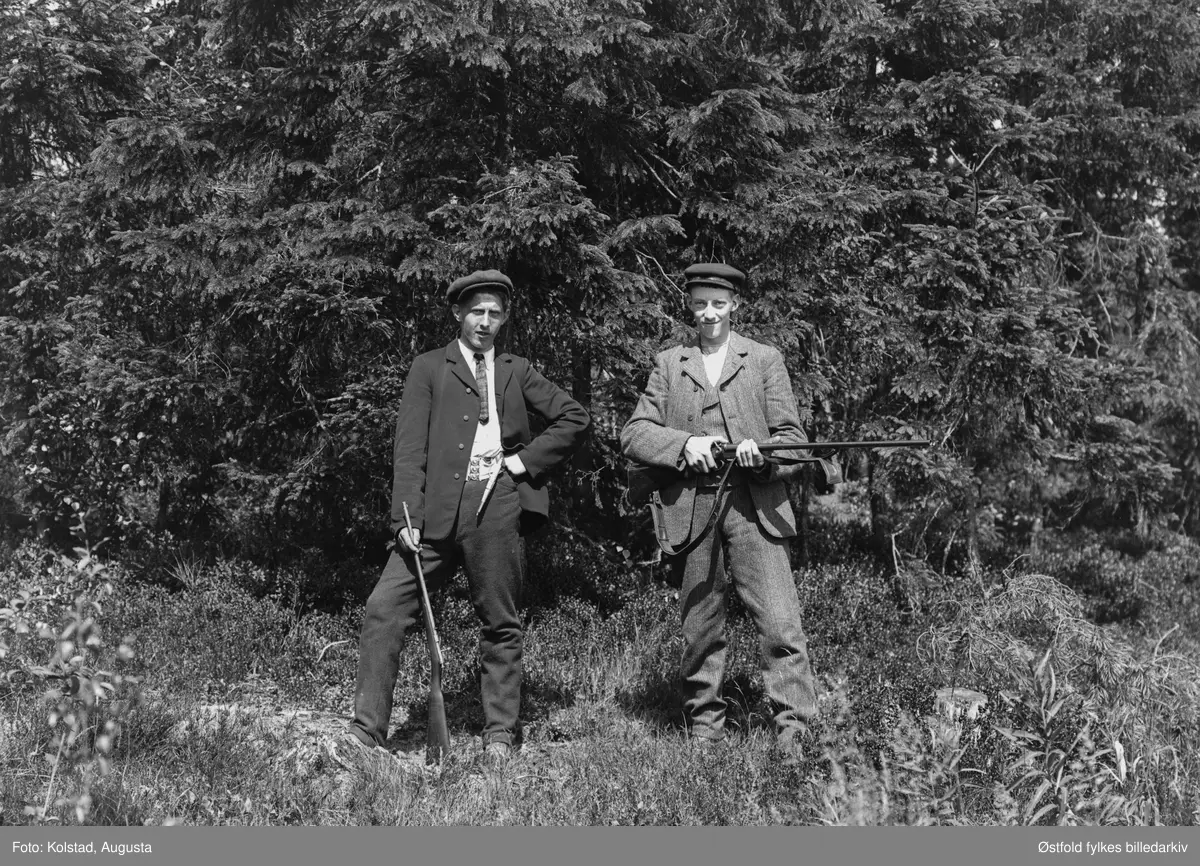 To jegere med våpen, ca. 1910-20, Til høyre Karl Hagbart Hansen Solvold (f. 1889) sønn av Hanna og Hans Anton Kristiansen, Askim. 
Karen til venstre (ukjent) har en fin tollekniv i beltet, mulig Totenkniv, kanskje det er bein i skaft og slire, vanskelig å si sikkert men materialet ser veldig lyst ut. I tillegg har han et finkalibret gevær, trolig kaliber .22, også kalt salongrifle.  Karl til høyre har et dobbeltløpet haglegevær, sideligger, med utenpåliggende haner. Brukes til fugl- og harejakt.
Tor Ulsnæs 2018