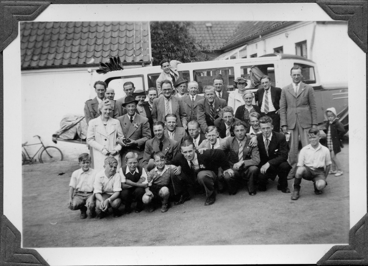 Oppstilt gruppefotografi foran buss. Bygninger i bakgrunnen.