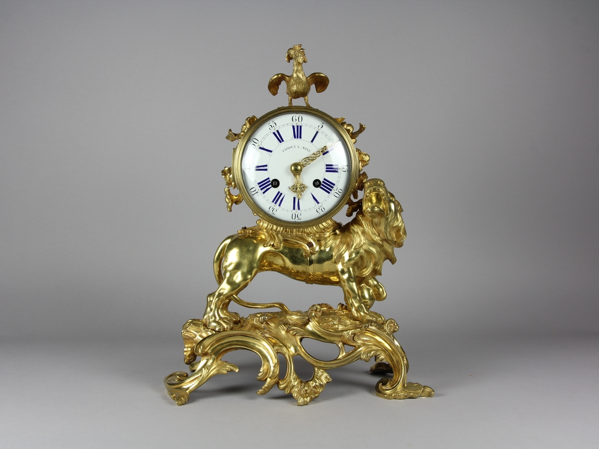 Urhuset i form av en tunna som står på ett rytande lejon med ena foten på ett klot på ett genombrutet rocailleornament. Ovanpå tunnan står en galande tupp, på sidorna rosor och växter.