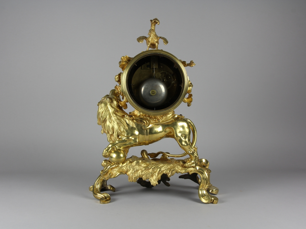 Urhuset i form av en tunna som står på ett rytande lejon med ena foten på ett klot på ett genombrutet rocailleornament. Ovanpå tunnan står en galande tupp, på sidorna rosor och växter.