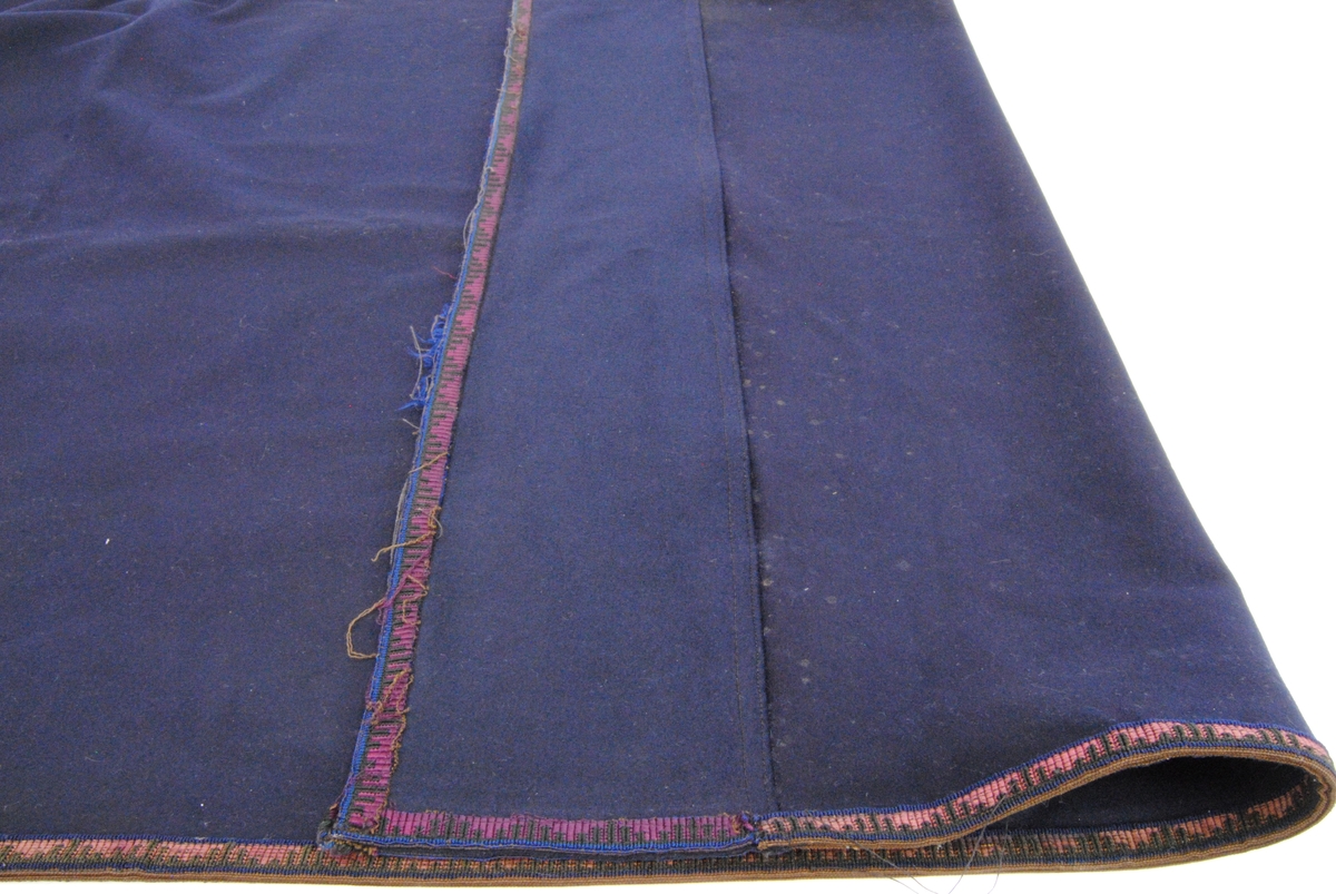 Ett draperi av mörkblå filt med en kringgående fastsydd bård. Bården har en enkel dekor som består av blå och svart tråd som vilar mot en textil som är röd/purpur färgad. Tyget är blekt.

Överst på draperi har det en gång suttit sex stycken fästen för att kunna hänga upp draperiet. Fästena finns idag inte kvar men man kan se var de har suttit. Längst ner på draperiet kan man se att draperiet är skarvat och att där sitter ett likadant tygstycke som draperiet är gjort av men att det är betydligt mindre blekt. Det kan hända att gardinen är förlängd eller att en nött bit, som har släpat i golvet, har klippts bort och ersatts.
