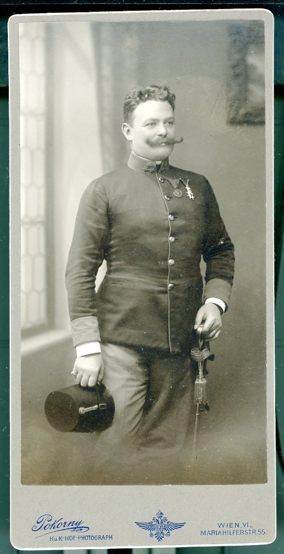 Kabinettsfotografi: Österrikisk-ungersk överste med stor mustasch och medaljer på bröstet. Uniformsmössan i ena handen och den andra på värjan.