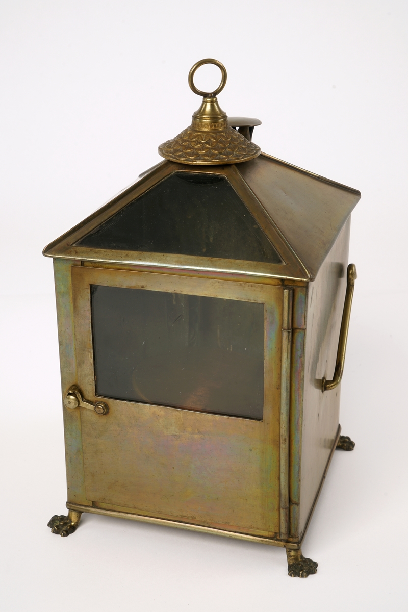 Firkantet kompasshus av metall med dør med vindu av glass. Døren kan låses med krok. Fire forsirede føtter av metall.  Tak som skråner til alle fire sider med vindu på takets forside. Luftavtrekk. Toppen av taket er utstyrt med forsiret deksel med bærering. To støttekroker, èn på hver side. Inne i huset er det to stearinlysholdere med metallfjær-innretning. Mellom disse er det fastmontert et metallrør.
Videre medfølger det to støtteklosser av tre for kompasset. Kompasslokk følger også med.