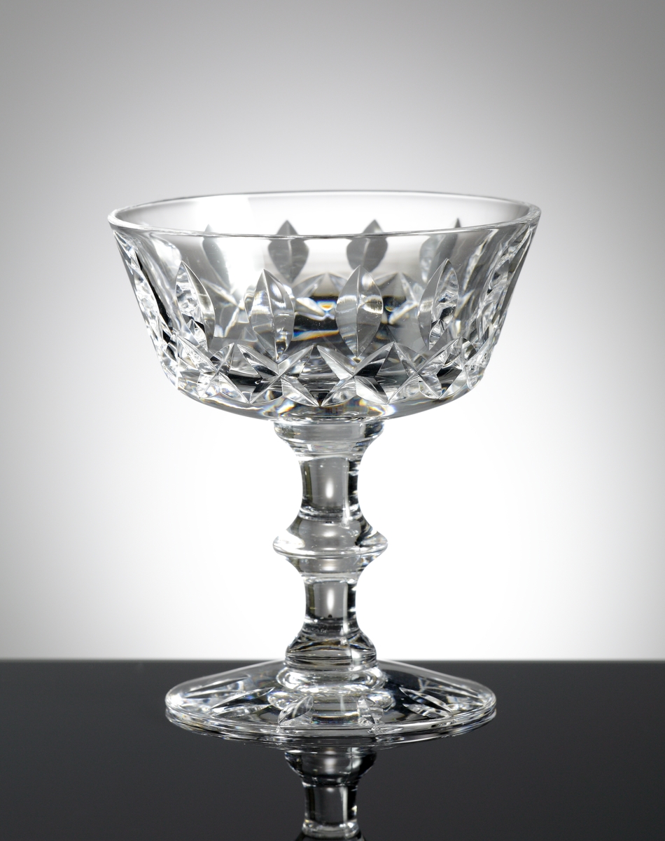 Konformad låg kupa av relativt generösa mått, ben med knapp.
På kupan stående skärslipade "spetsiga ellipser", nederst på kupen en bård av brillianter. Runt foten slipade "spetsiga ellipser".
Helkristall med högt blyinnehåll som ger tyngd åt glaset.
Fotografierna: David Lönnquist under sliparbetet. På gruppbilden står Lönnquist längst till höger.