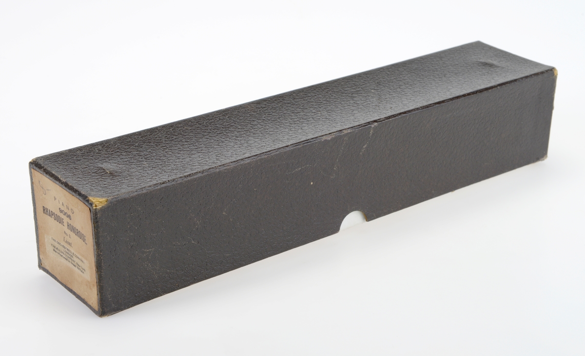 Rull til selvspillende piano med tilhørende eske. Musikkrullen er av hvitt papir og er rullet opp på en spole av tre der endestykkene er malt svart. I hver side er det metallfester for innsetting i selvspillende piano. På den første delen av rullen er det limt på en etikett med informasjon om musikkstykket. Etiketten er grå med svart skrift. På denne etiketten er det limt på en mindre rosa etikett med informasjon om forhandleren. Deretter er det trykt/stemplet informasjon om patent i Storbritannia, USA og Frankrike. I enden er det limt på en hvit tekstilbit. I denne er det festet en liten metallring. Esken er laget av papp og er i to deler, esken er trukket med hvitt papir mens lokket er trukket med brunt papir.  Papiret på lokket har blindpreg. Foran på esken er det en brun etikett med påtrykt tekst med informasjon om musikkrullen, se "Påført tekst/merker".  Nede i esken er det limt fast en trekloss med hakk i hver ende, dette for at rullen skal ligge stødig i esken.