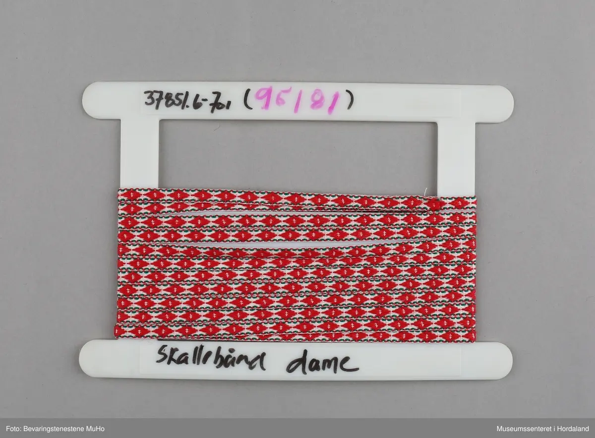 Vevd band, produsert ved bandfabrikken Trengereid Fabrikker i Bergen. Bandet er skalleband til samedrakt, dette til dame.