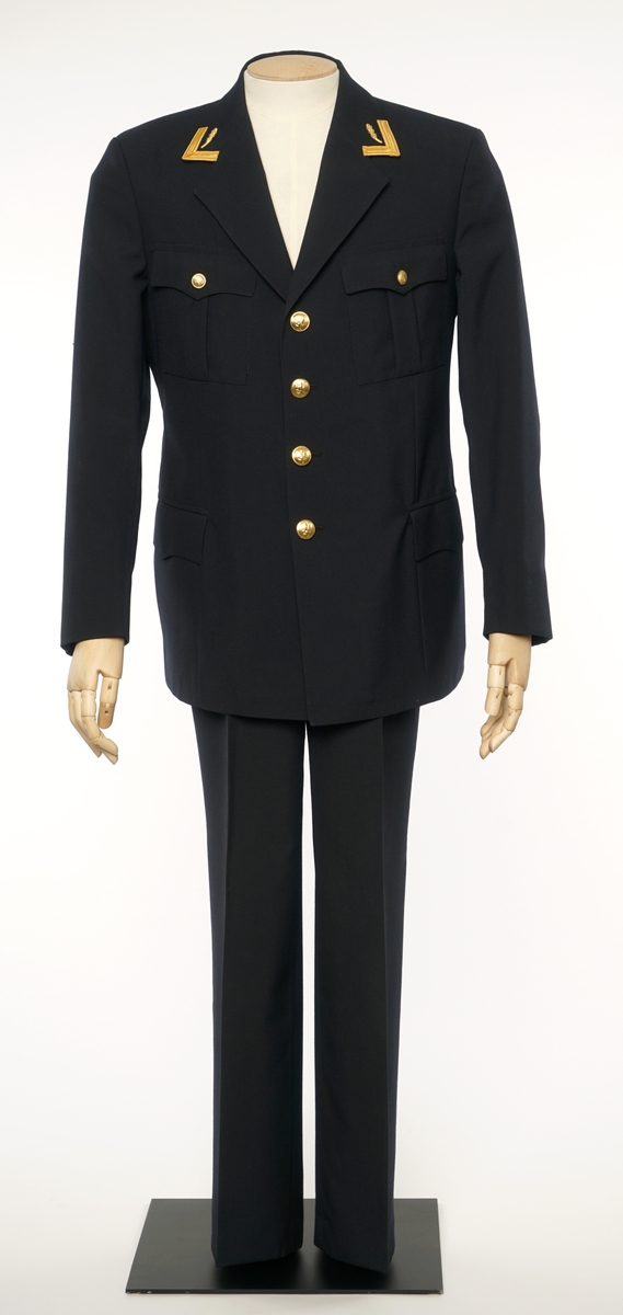 Mørkblå jakke enkelspent med fire riksløveknapper. Liggende krave med en eiksblade distinksjon med gullbånd på hver side. Stoffet er et enkelveved stoff, antatt en blanding av ull og syntetisk fiber. Jakke er foda med antatt syntetisk stoff, mørkblå. 
Bukser av samme stoff.