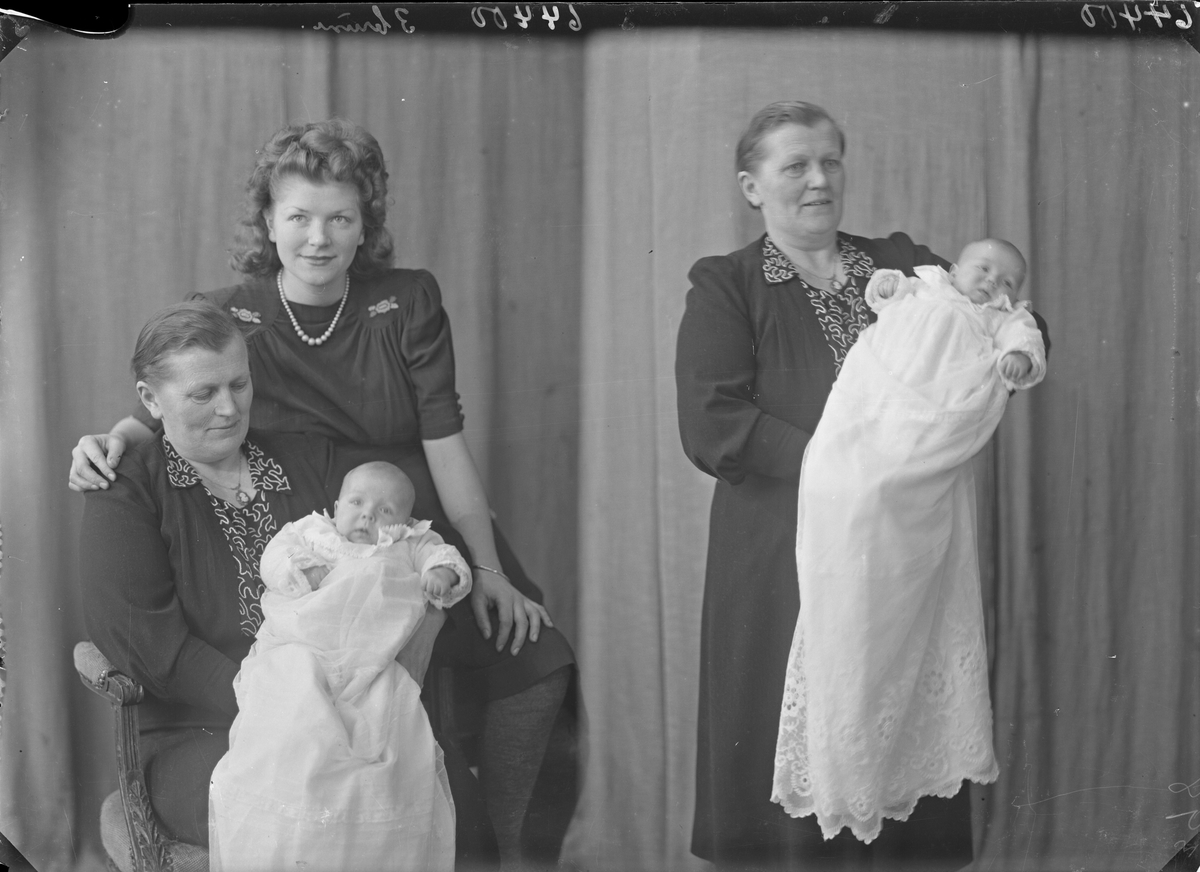 Gruppebilde. Familiegruppe på tre. Eldre kvinne i mørk kjole med brodert front med dåpsbarn i hvit dåpskjole på fanget. Ung kvinne i mørk kjole med broderte blomster og perlekjede. Tre generasjoner - bestemor, mor og barn. Bestilt av Ellen Jakobsen. Sørhaugt. 91