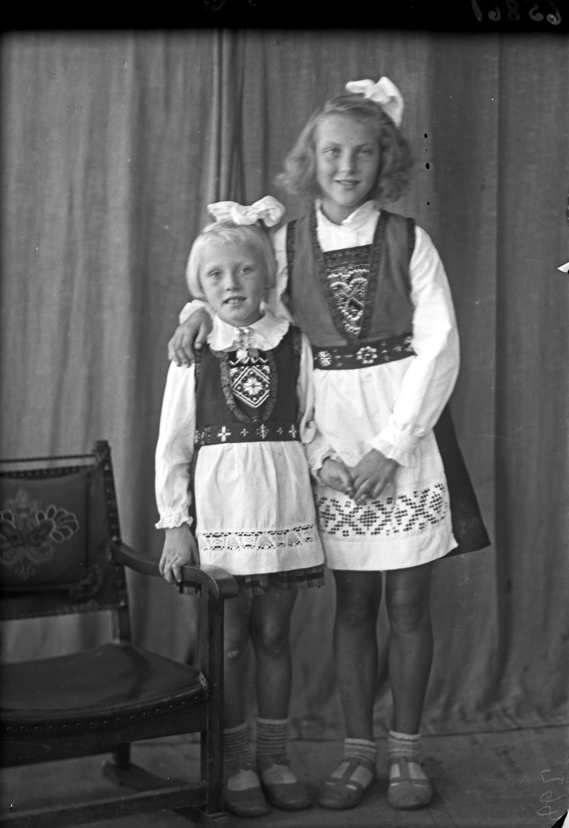Gruppebilde. Familiegruppe på to. To unge piker i nasjonaldrakt med sløyfer i håret. Søstre. Bestilt av Erling Nilsen. Strangt. 181