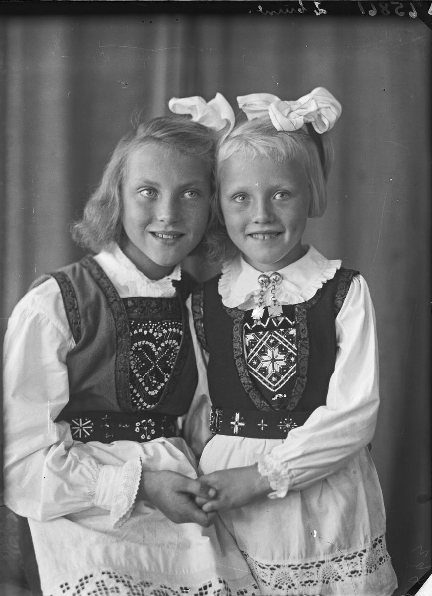 Gruppebilde. Familiegruppe på to. To unge piker i nasjonaldrakt med sløyfer i håret. Søstre. Bestilt av Erling Nilsen. Strangt. 181