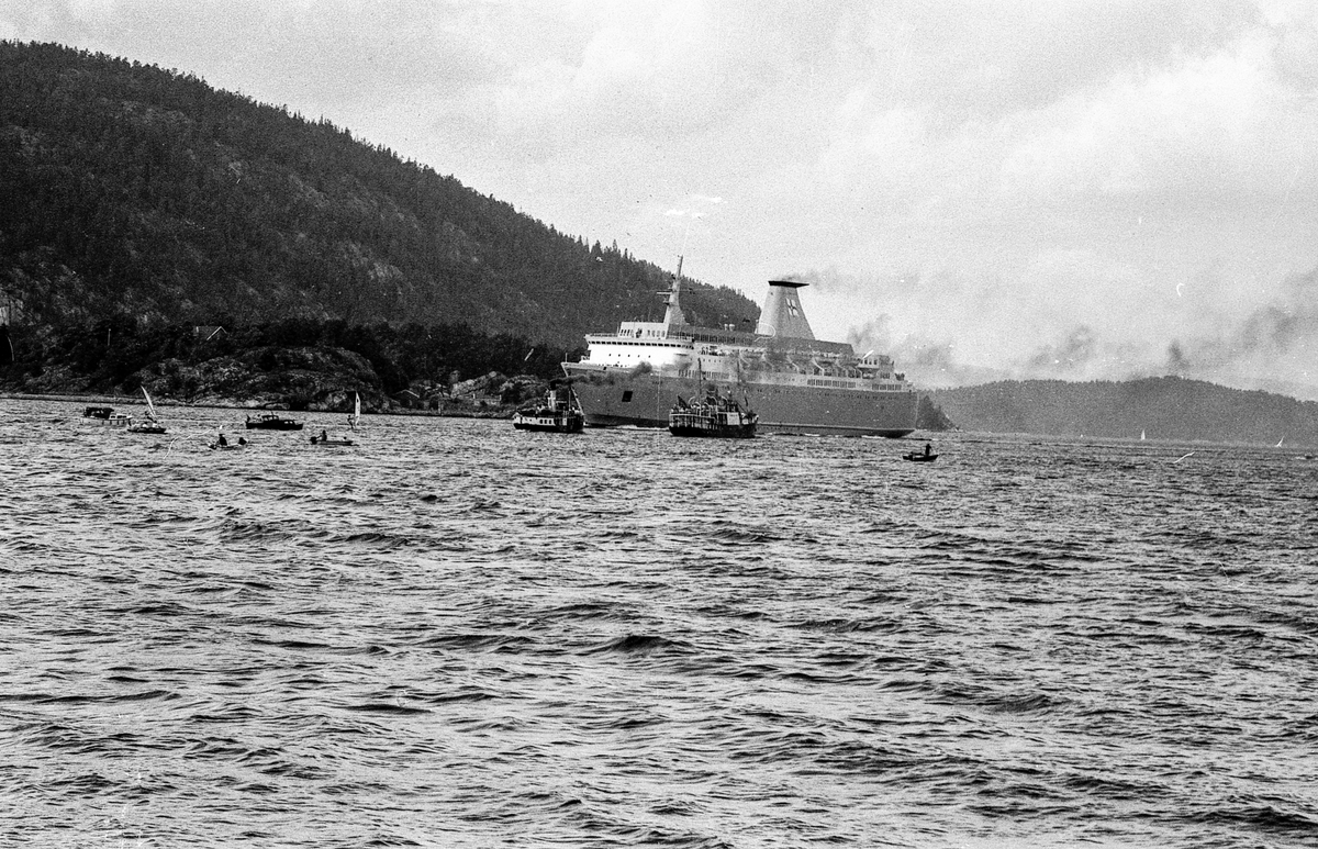 Drøbaksfjorden, sundet ved Oscarsborg. Tre menn på brygga ser på båtene med kikkert. Sandtaket og småhus på Hurum.
Fotograf: ØB Rønning