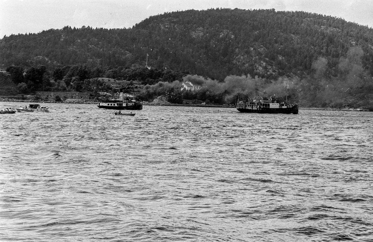 Drøbaksfjorden, sundet ved Oscarsborg. Tre menn på brygga ser på båtene med kikkert. Sandtaket og småhus på Hurum.
Fotograf: ØB Rønning