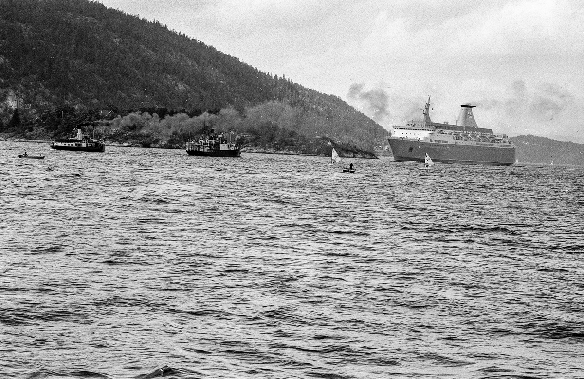 Drøbaksfjorden, sundet ved Oscarsborg. Tre menn på brygga ser på båtene med kikkert. Sandtaket og småhus på Hurum.
Fotograf: ØB Rønning