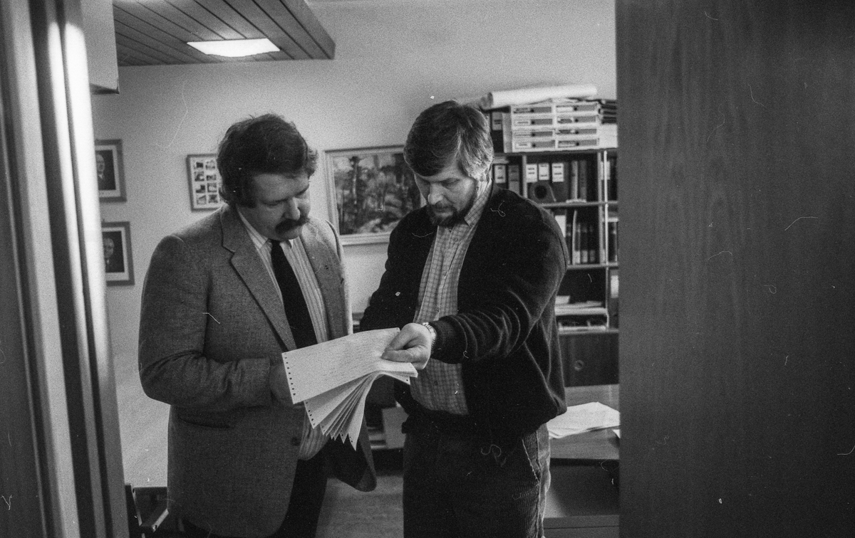 Ås trygdekontor stenger som en aksjon for å få utbedret dataanlegget som de er helt avhengige av. Salgsjef Olav Dalåsen i Norsk Data i samtale med trygdesjef Jan Espeland står i døråpningen med papirer.