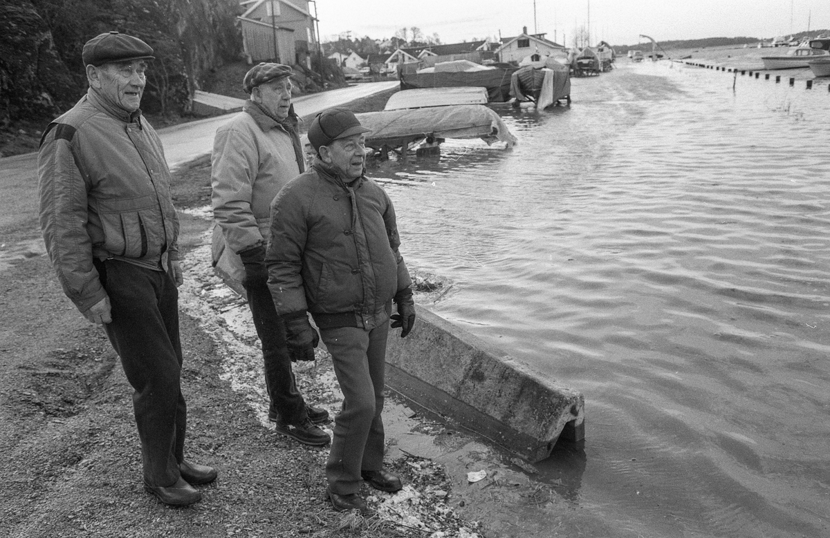 Flom ved marinaen i Son. Sjøen går opp til brygga og over trapper og gjerder. Tre menn ser på. Karlsen, Jacobsen og Hansen.
