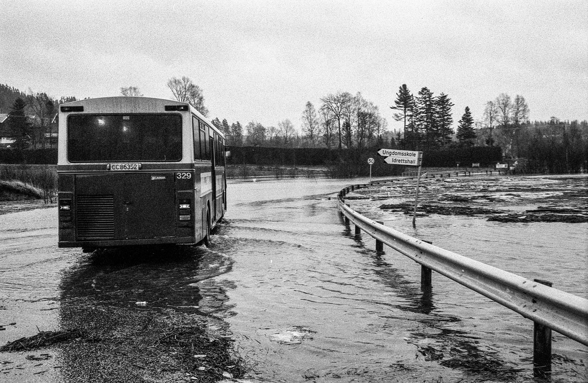 Flomskader på veiene, Riksvei 120, Ytre Enebakk. Vannet flommer over veier og jorder, biler kjører så vannspruten står.